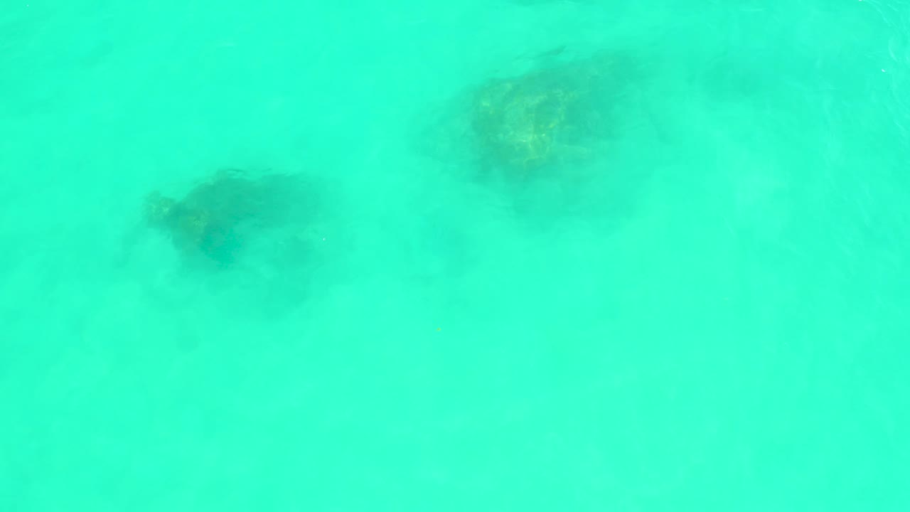 Turquoise water over dark underwater coral formations.