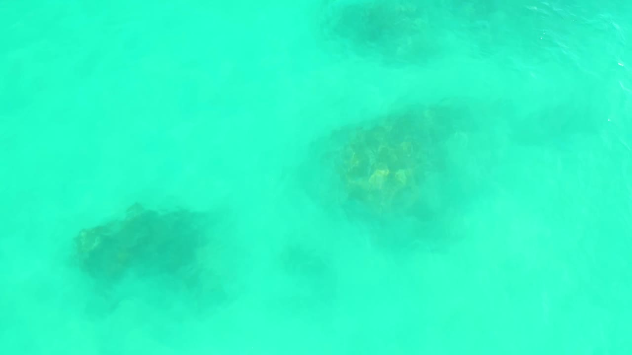 Turquoise water at Marquis Los Cabos reveals multiple underwater coral or rock patches through light surface haze, with no visible people.