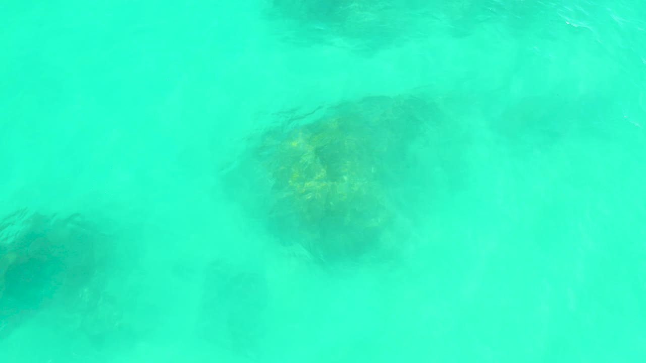 At Marquis Los Cabos, dark underwater rock shapes sit beneath milky turquoise water, with a small bright glint near the left side and no visible people.