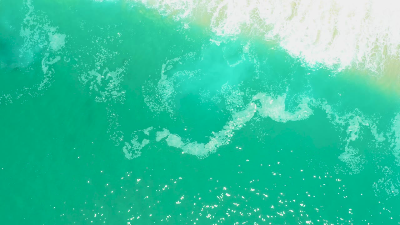 Top-down Marquis Los Cabos water frame with dense white surf foam near the top and softer foam trails over turquoise water below, with no visible people.