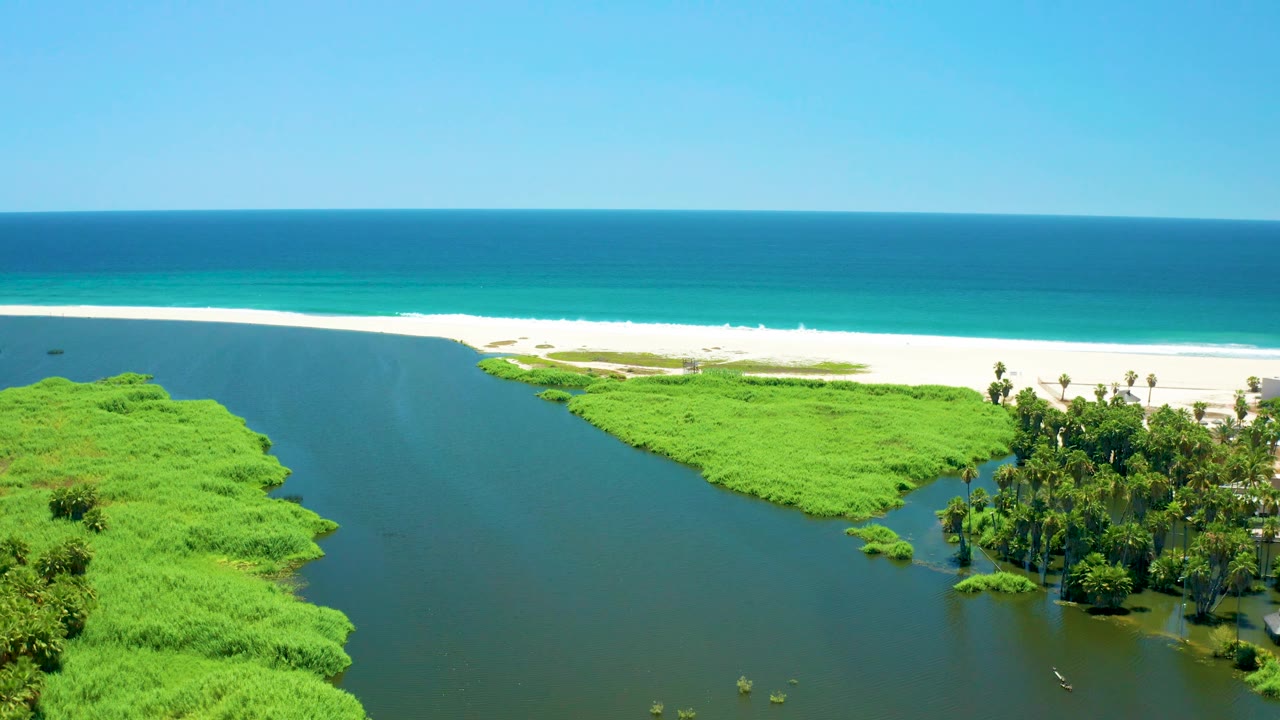 Lagoon and green vegetation below a sandy beach and turquoise ocean.
