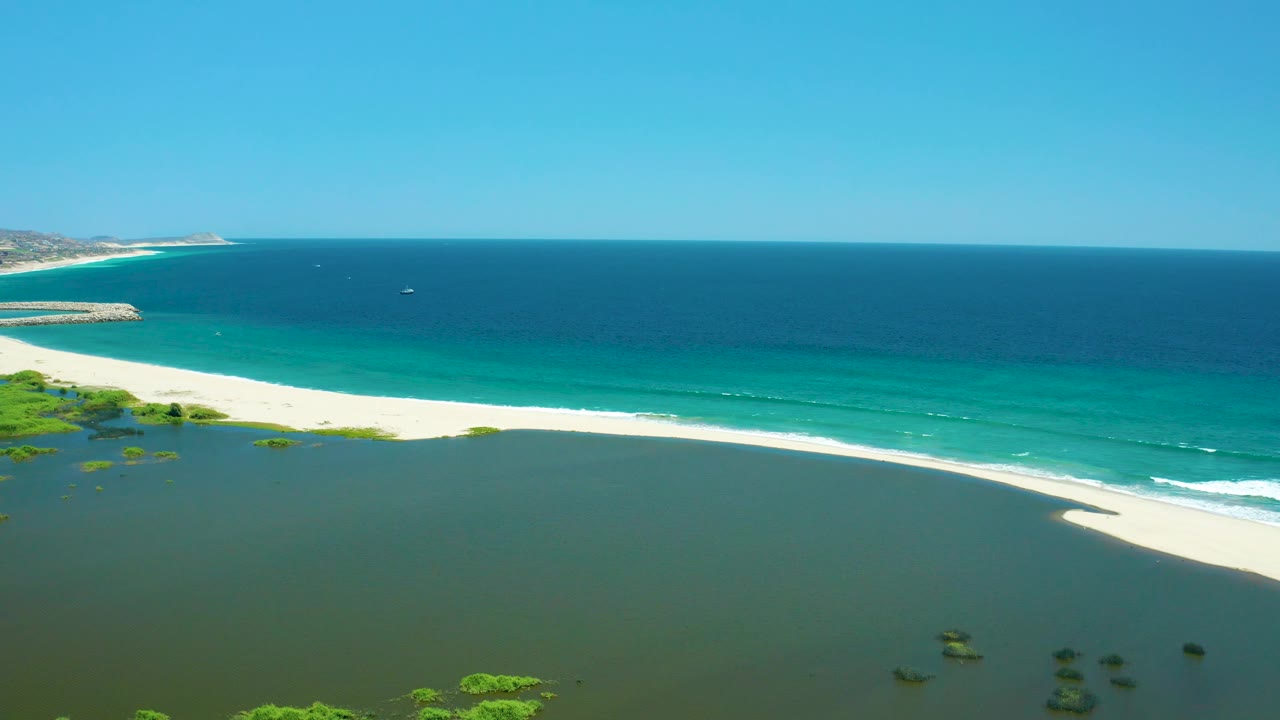 Aerial view of broad lagoon foreground, pale beach, turquoise surf, and blue ocean horizon.