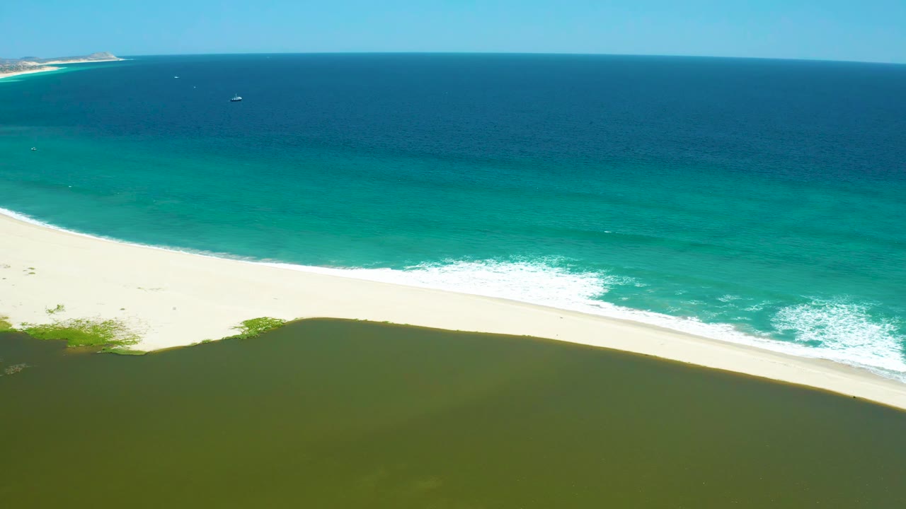 White sand beach between dark lagoon water and turquoise ocean waves