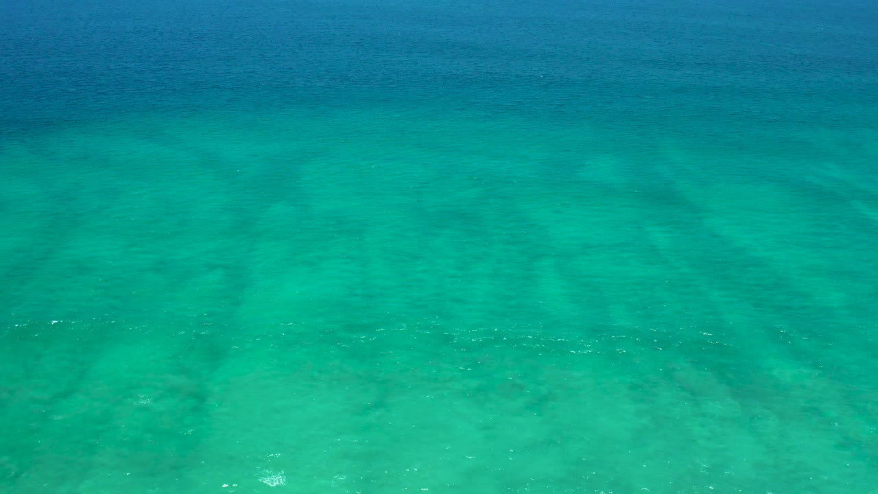 Blue-green shallow ocean water at San Jose Del Cabo Estuary shows a sandy bottom beneath small surface ripples, with no visible people.