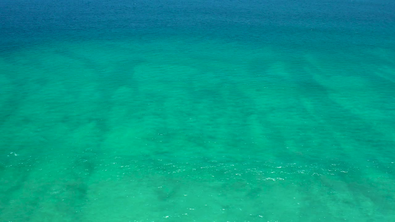 A shallow turquoise ocean surface covers a visible sandy floor at San Jose Del Cabo Estuary, with soft ripple lines and no visible people.