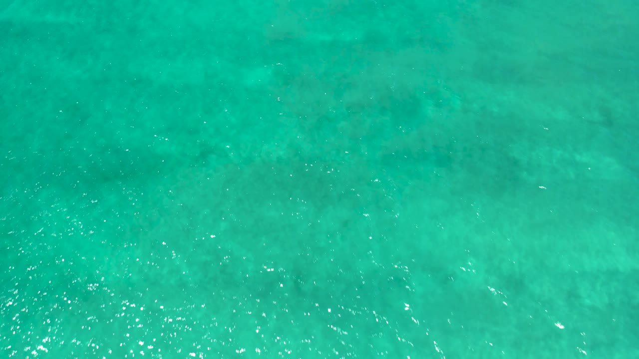 Aqua-toned ocean surface at San Jose del Cabo Estuary shows soft ripples, muted darker shapes beneath the clear water, and no visible people.