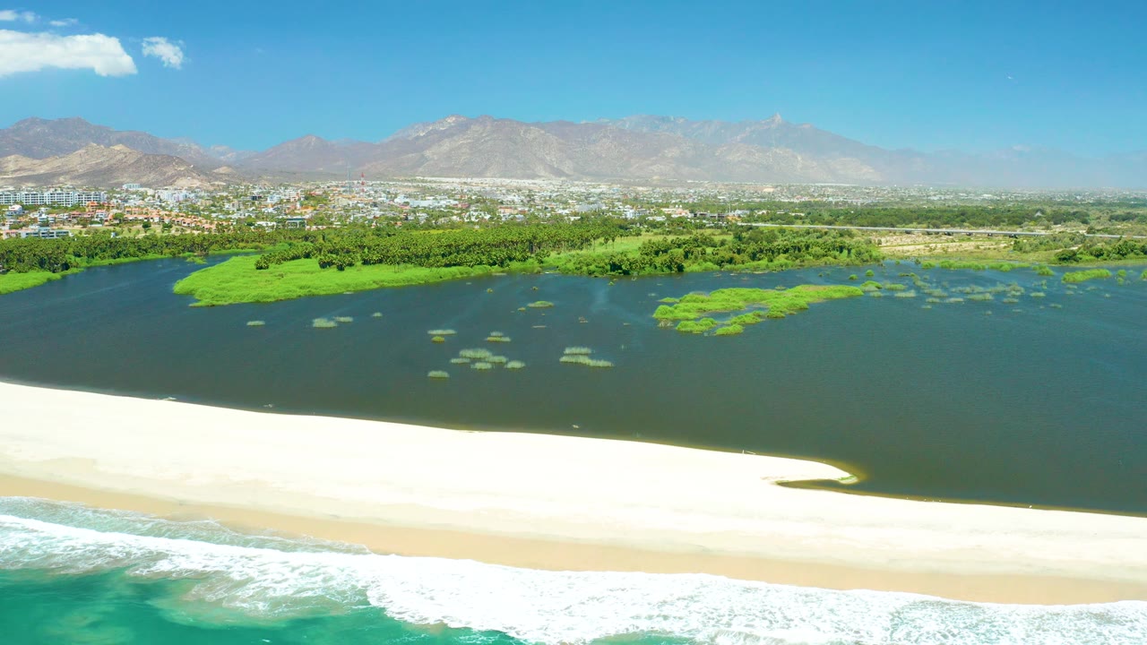 Lagoon and beach aerial with ocean foam at the lower edge and mountains beyond.