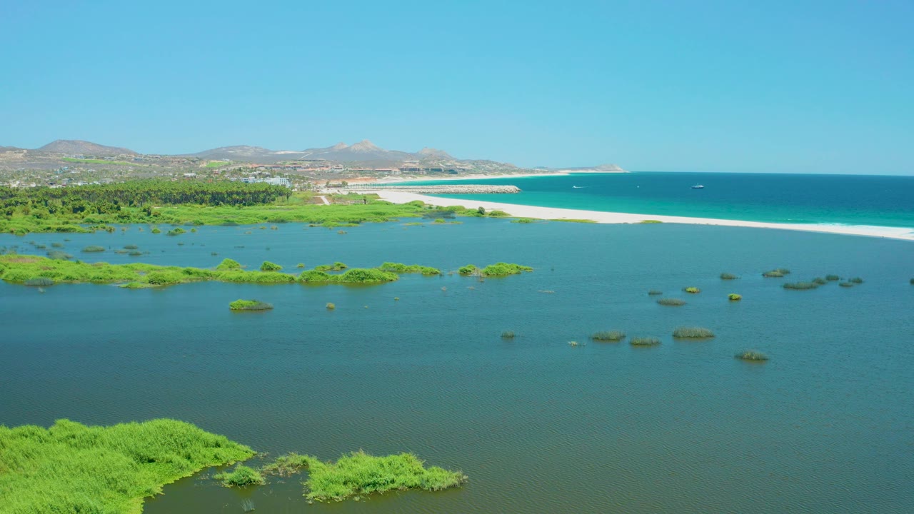 At three seconds, green marsh in the lower left foreground leads into open lagoon water, a bright sandbar, turquoise ocean, low hills, clear sky, and no visible people in the San Jose del Cabo Estuary view.