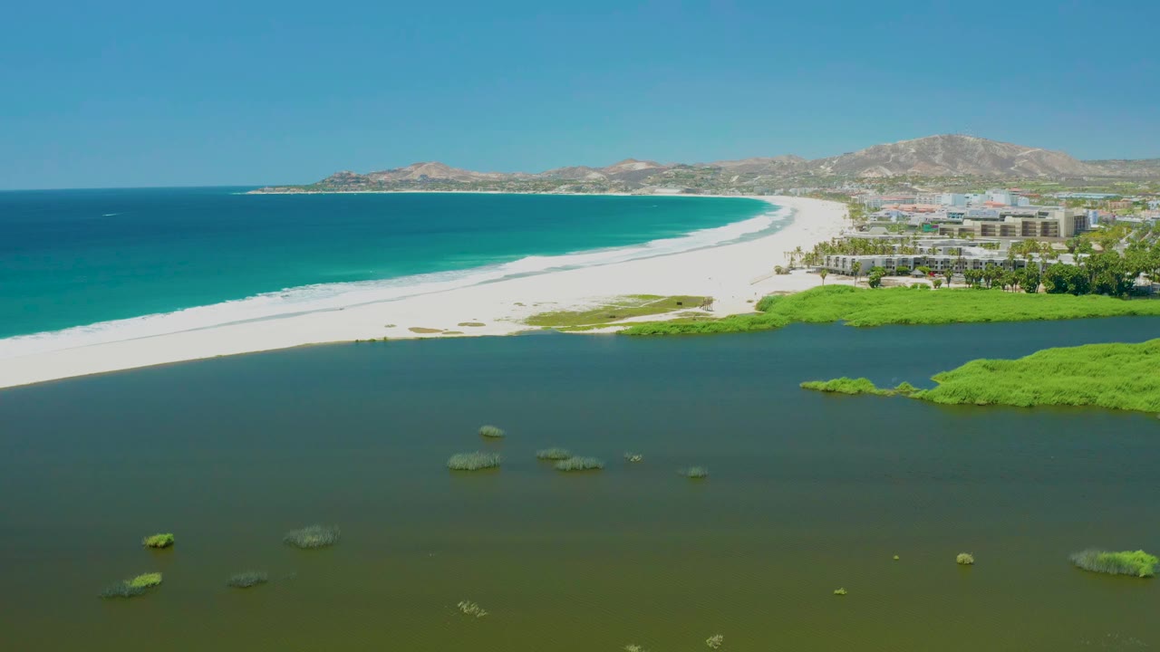 Aerial view of lagoon, white sand beach, turquoise ocean, coastal buildings, and hills.