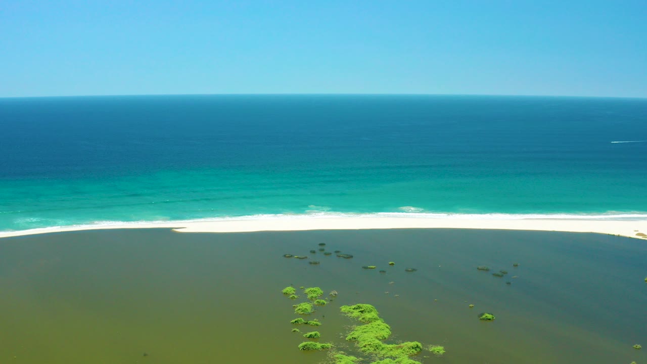 Aerial view of green lagoon water, sandy beach, turquoise ocean, and blue sky.