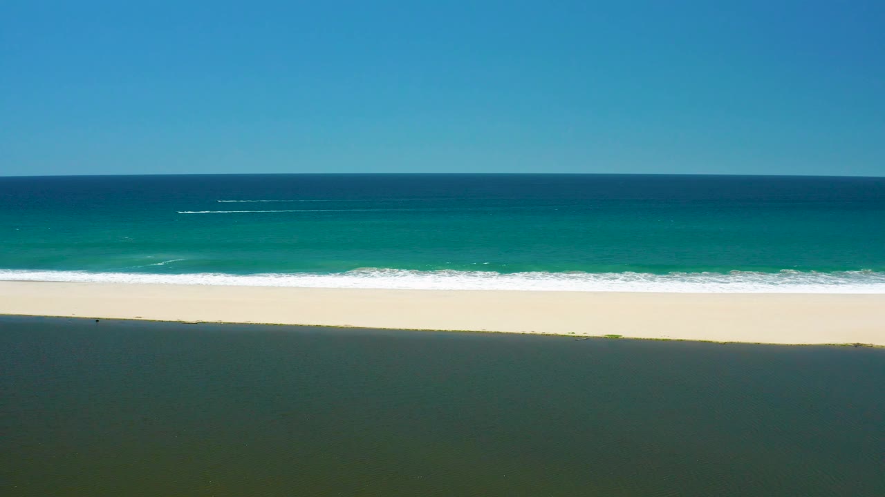 High coastal view with turquoise water, foam band, empty sand, and blue sky