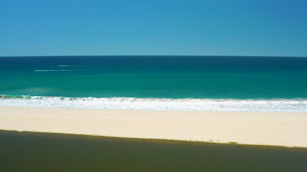 Elevated view of turquoise ocean waves reaching a pale sandy beach.