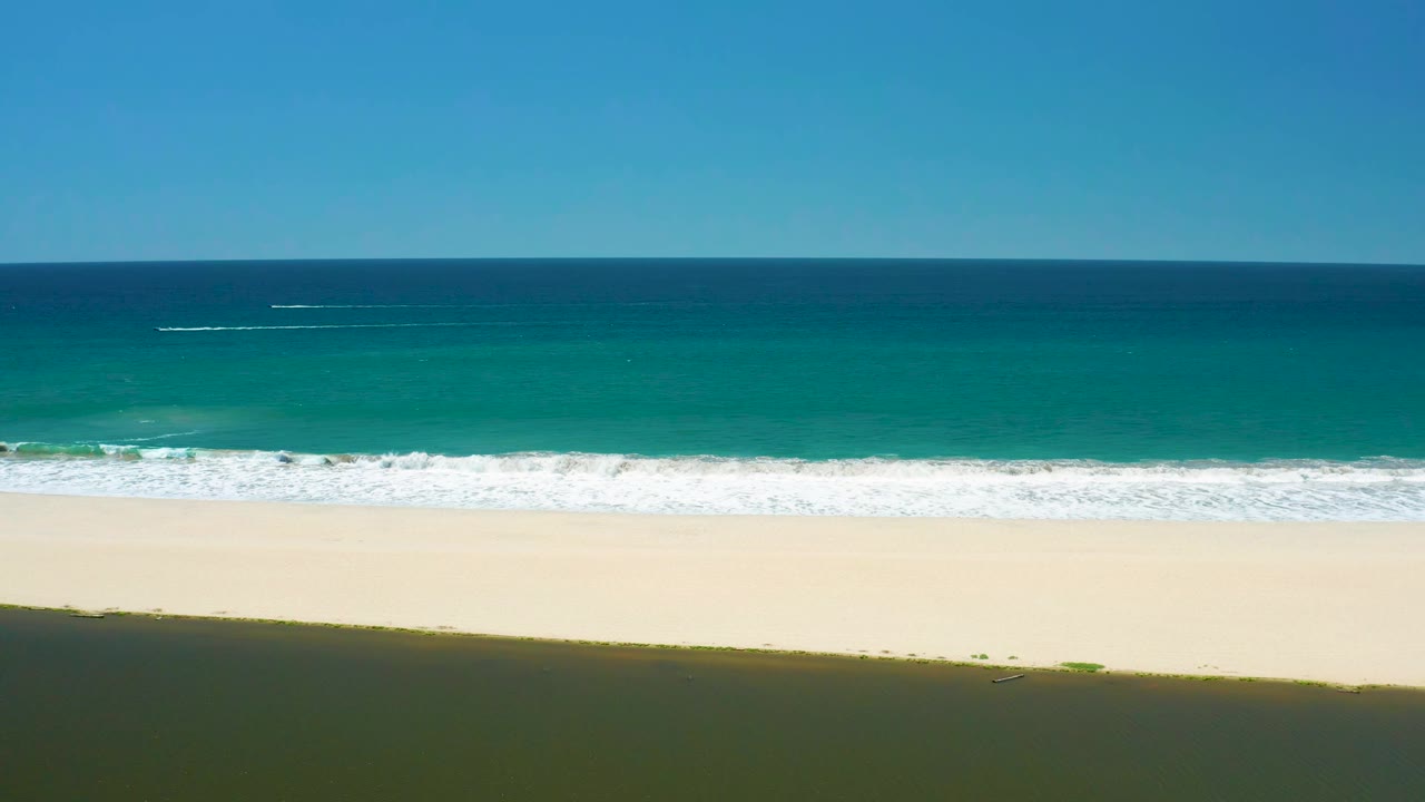 At 0:01, the surf band sits lower on the San Jose Del Cabo Estuary beach, with more pale sand visible beneath the foamy water and no visible people.