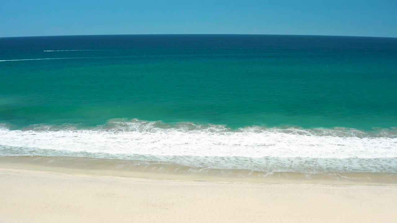 Aerial shoreline view with a long white wave line crossing turquoise water.