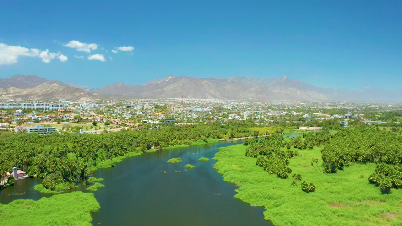 River and green estuary banks with city buildings and mountains beyond.