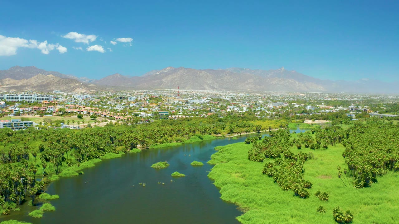 Fourth frame presents the San Jose del Cabo Estuary with the river running along the lower left, thick green vegetation across the center, distant buildings and mountains, and no visible people.