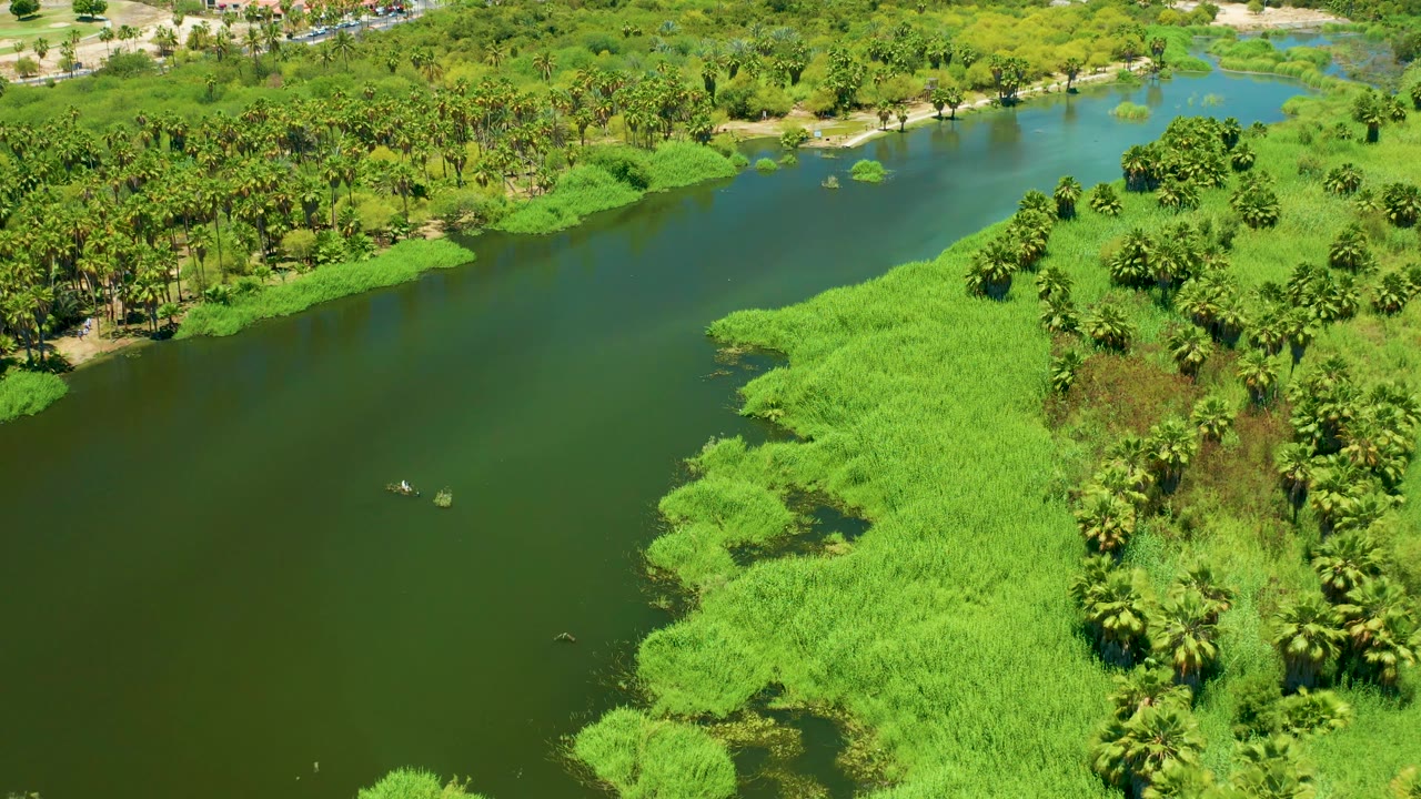 Drone view of a river bend with dense greenery and small boats.