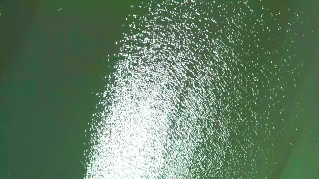 Sunlit green water with ripples and faint underwater shapes