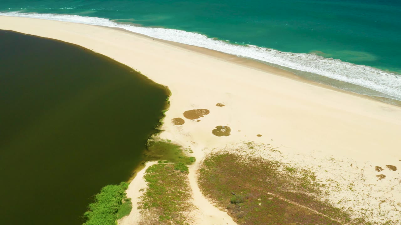 At 0:02, the San Jose Del Cabo Estuary shoreline appears as a broad band of pale sand between dark lagoon water and turquoise ocean waves, with no visible people.