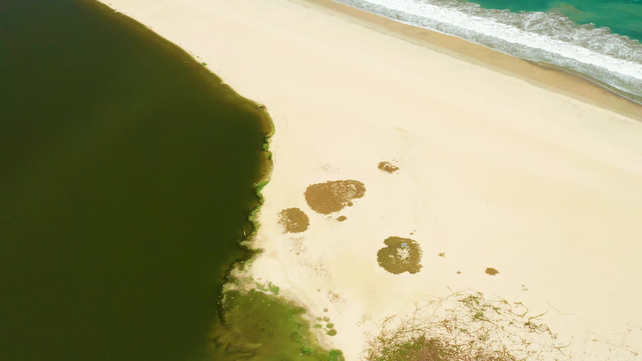 Aerial view over San Jose Del Cabo Estuary with the dark tidal pool still filling the left side, small brown patches on the sand, surf near the top edge, and no visible people.