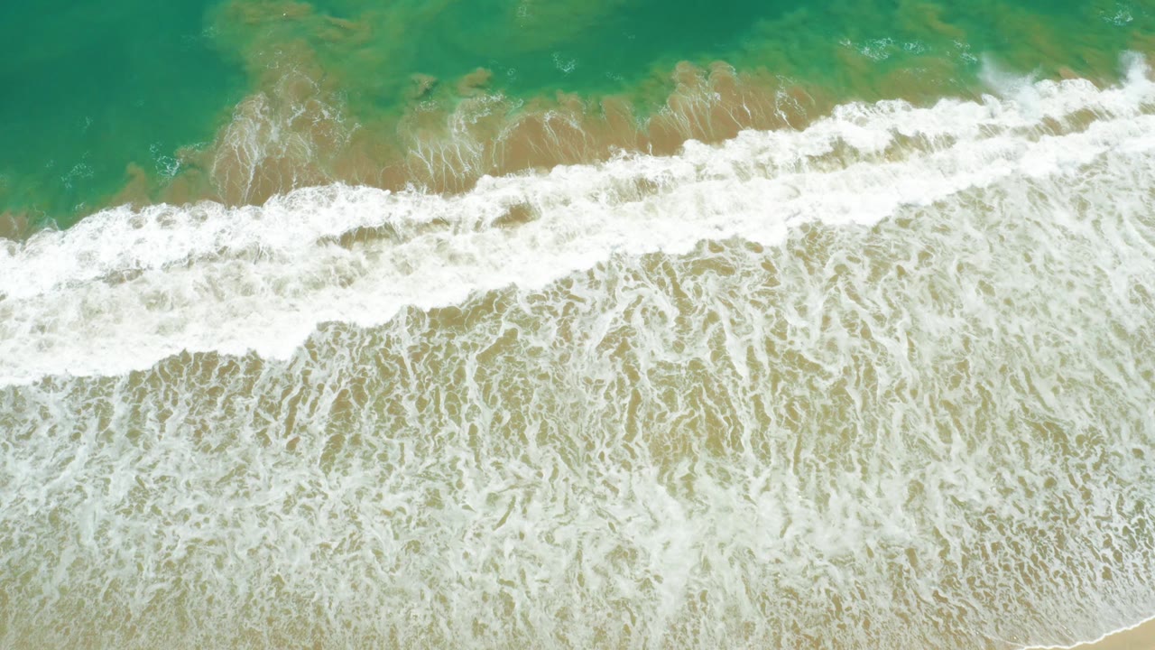 Aerial overhead view at San Jose Del Cabo Estuary with a broad white surf band, sandy shallows, turquoise ocean, and no visible people.