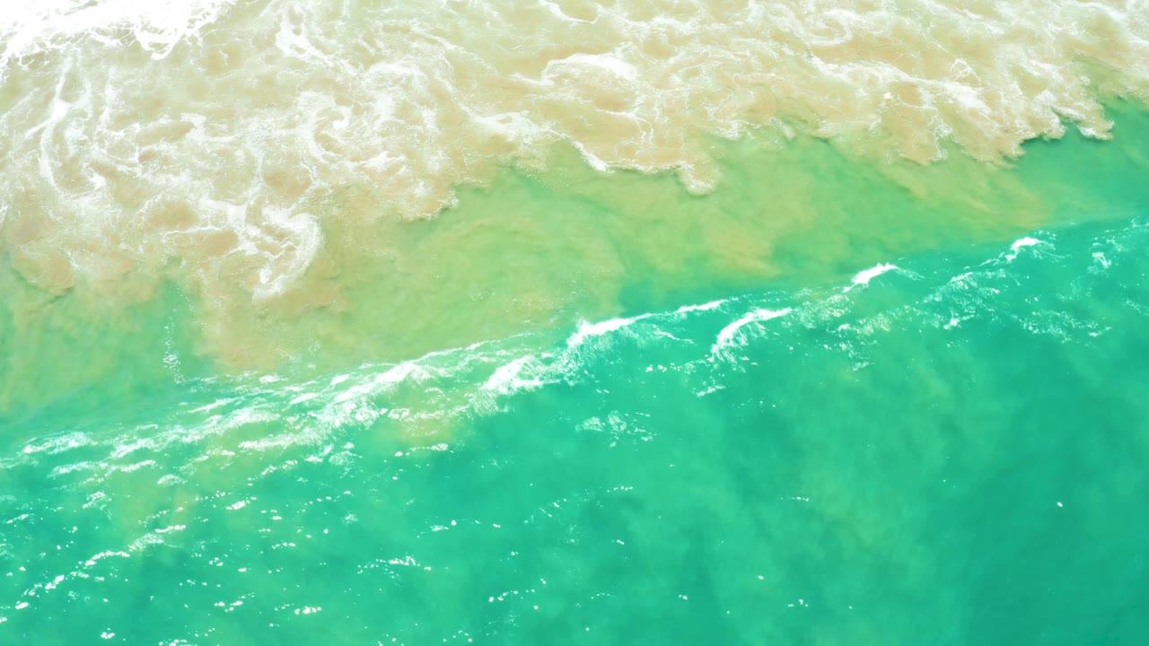 Diagonal breaking wave line crossing turquoise ocean water.