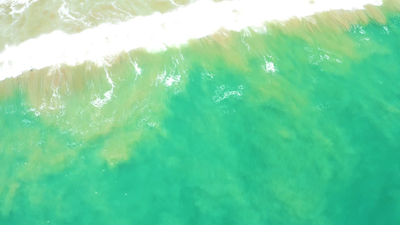 Overhead San Jose Del Cabo Estuary water frame with the foamy wave line thinning near the top and mottled green sand color visible below, with no visible people.