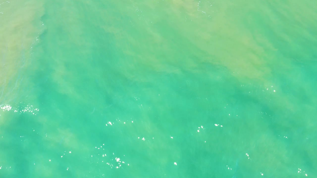 Turquoise ocean water with pale shallow patterns and small sun sparkles.