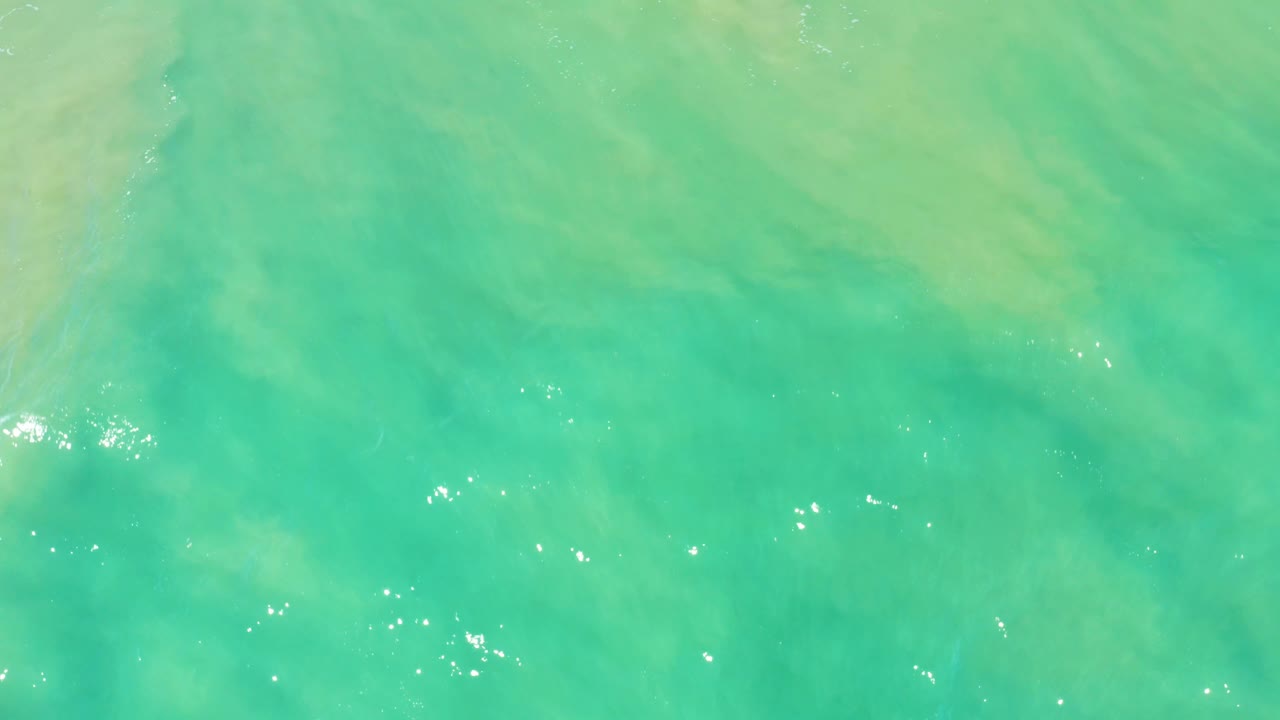 Clear green turquoise water at San Jose Del Cabo Estuary fills the frame, with faint seabed shapes and scattered white sun reflections, no visible people.