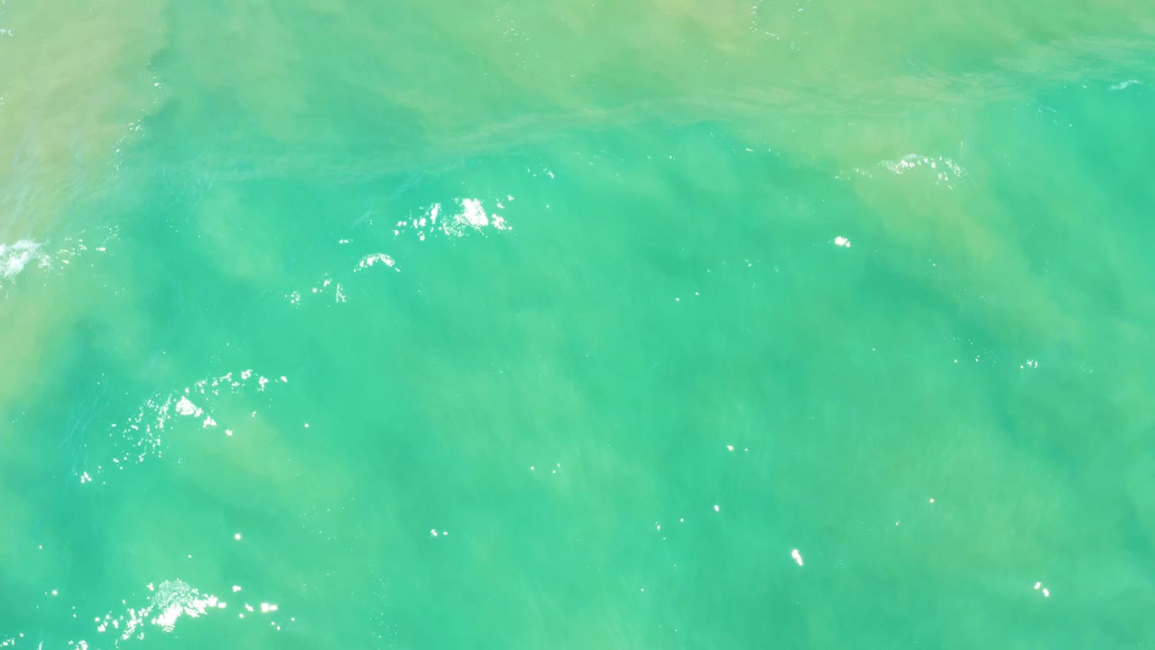 Bright turquoise ocean surface at San Jose Del Cabo Estuary shows a stronger cluster of white sun glints over shallow green water, no visible people.