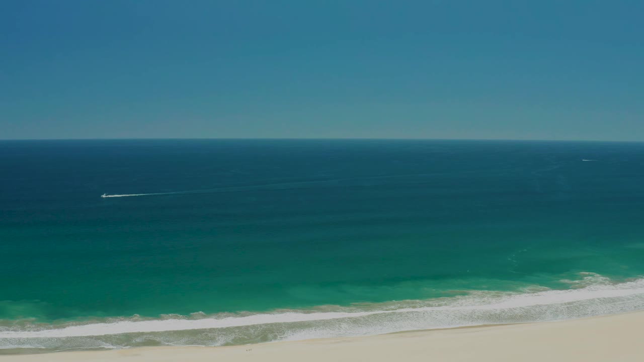 Ocean horizon above turquoise surf and pale sand.