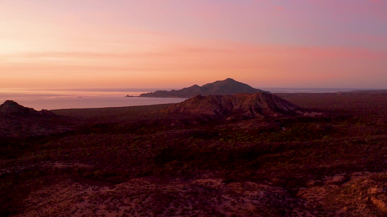Cabo Pulmo, Baja California Sur sunset view with dry rocky foreground, dark mountain ridge, ocean horizon, distant island form, and no visible people.