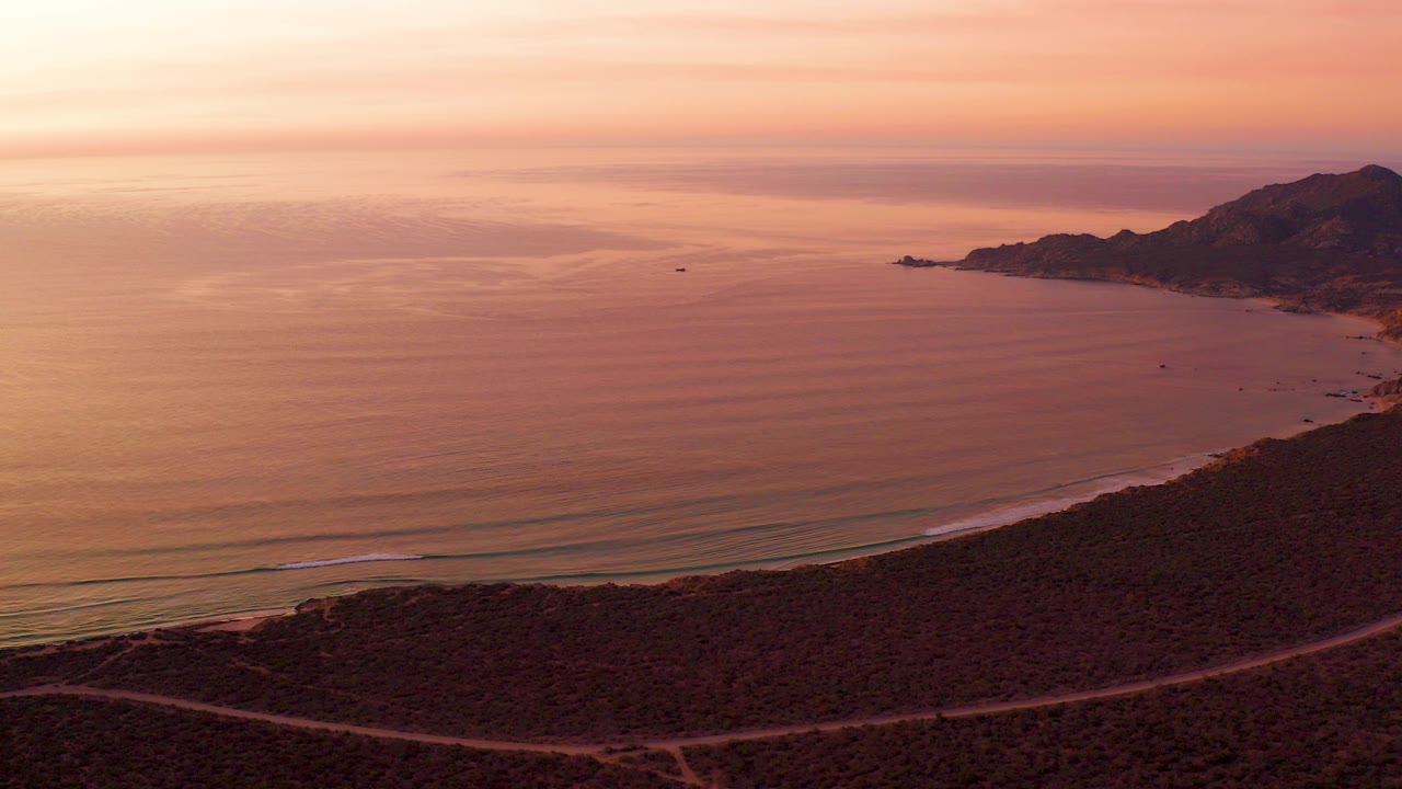 Aerial sunset view of ocean, beach, winding coastal road, and hills