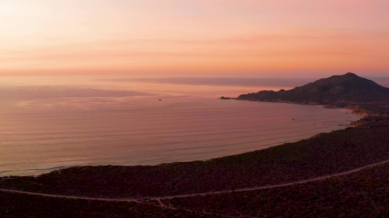 Pink sunset over ocean beside a mountain coastline