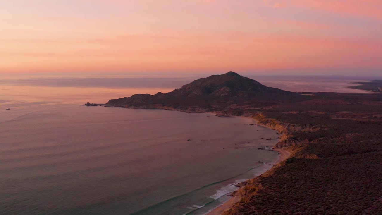Wide sunset coastline with ocean, hill, beach, and dark coastal vegetation