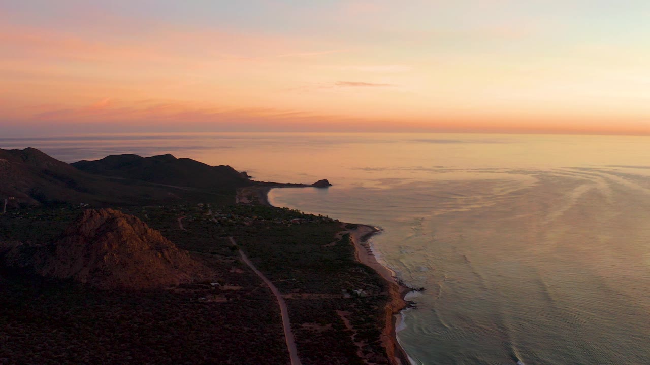 Aerial coastal sunset with hills, road, beach, and calm ocean