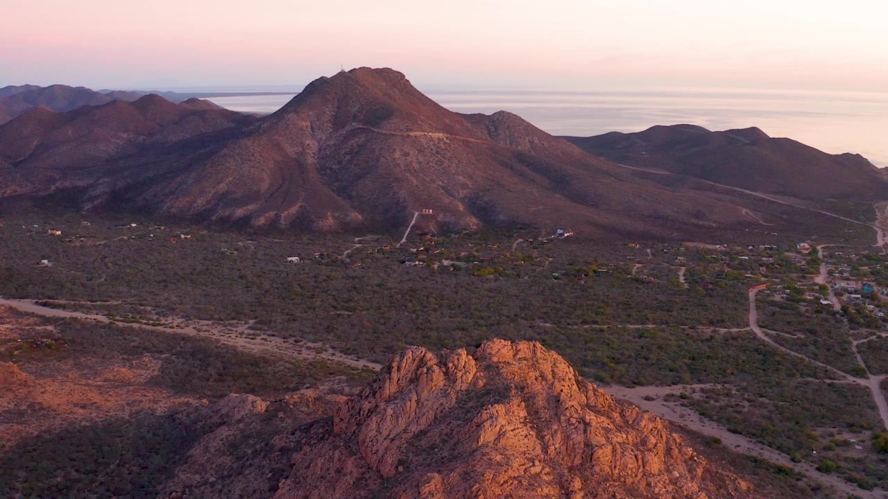 Desert valley and mountains at sunset with foreground rocks.