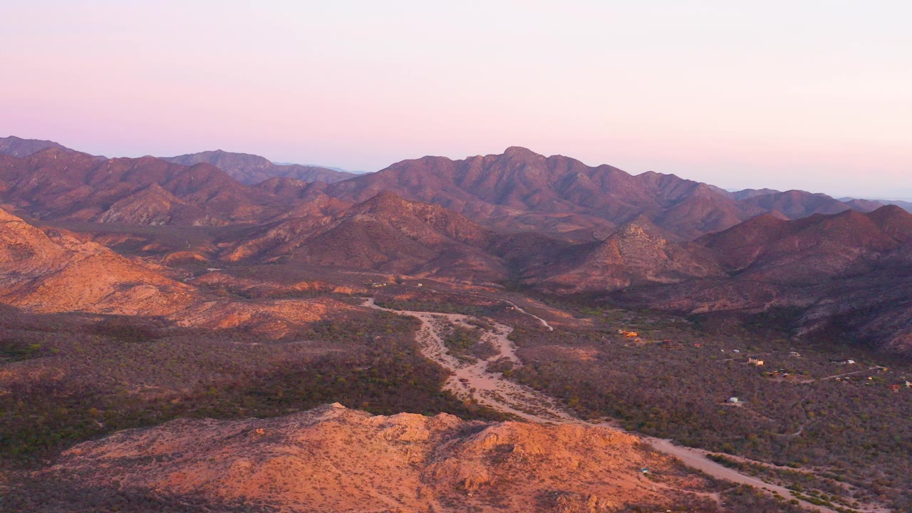 Aerial view of desert road winding through mountain valley at pink dusk light.