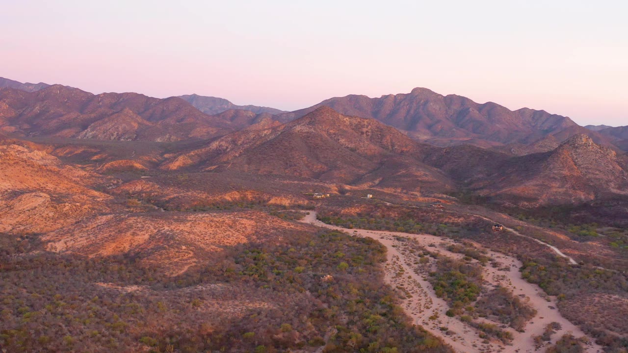 Cabo Pulmo aerial frame with the dirt road and dry wash more centered in the desert foreground, mountain ridges across the back, and no visible people.