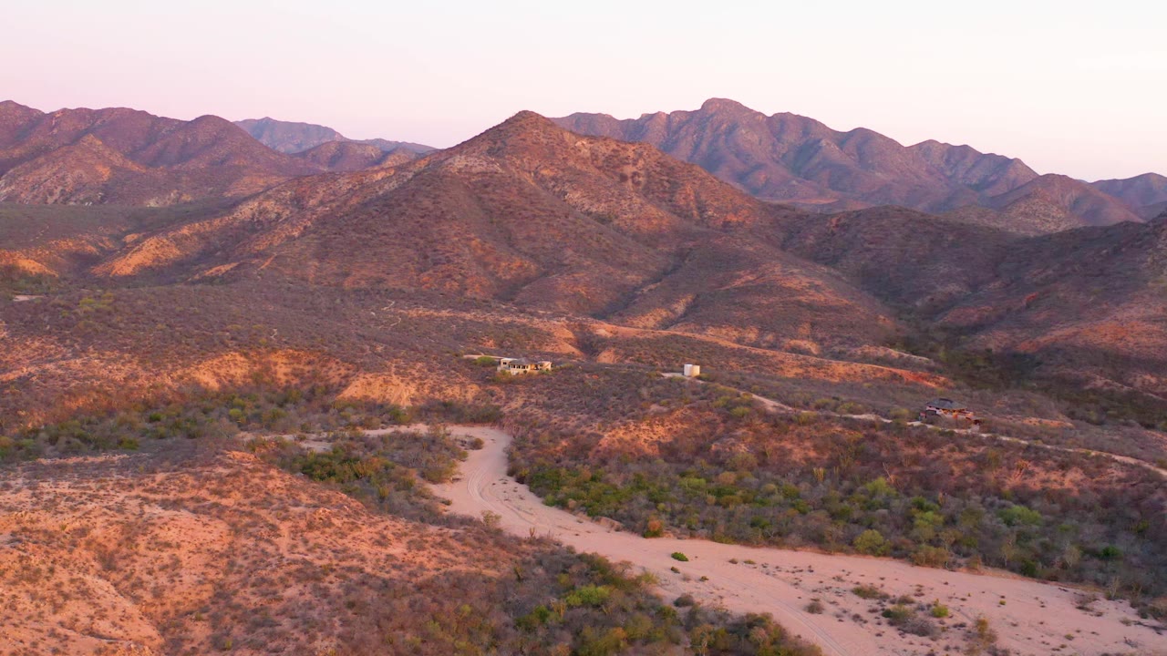 Desert hills and a pale dirt road below mountain ridges.