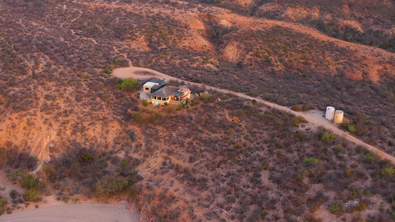 Aerial view across Cabo Pulmo, Baja California Sur with the house near the upper left, a road leading to tanks on the right, scrub vegetation, and no visible people.