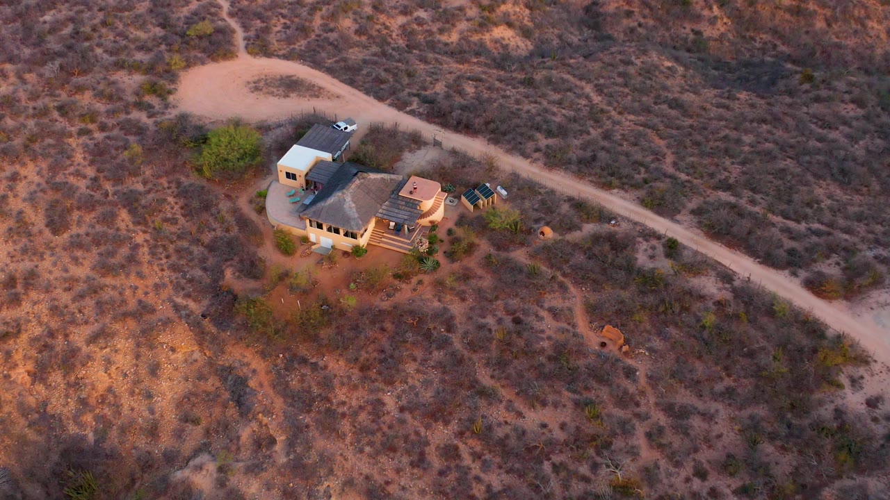 Closer aerial view of a remote house below a dirt road
