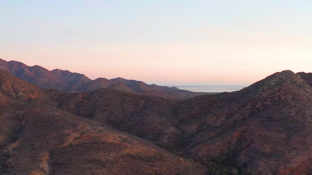 Cabo Pulmo mountain slopes fill the frame with darker peak silhouettes behind them and a soft pink dusk band near the horizon, with no visible people.