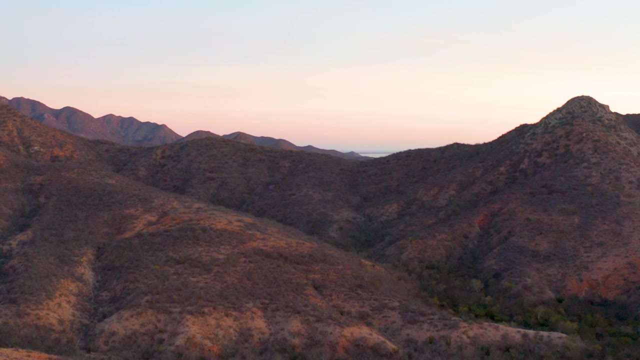 Cabo Pulmo aerial view with layered brown hills, a darker valley channel in the foreground, distant ridge silhouettes, and no visible people.