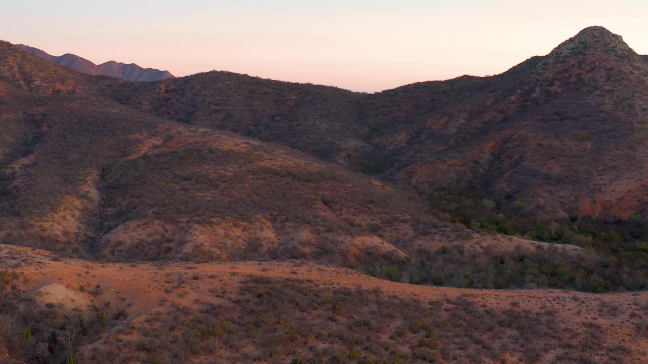 Cabo Pulmo, Baja California Sur mountain ridges in warm low light beneath a pink-tinted sky, with scrubby dry foreground and no visible people.