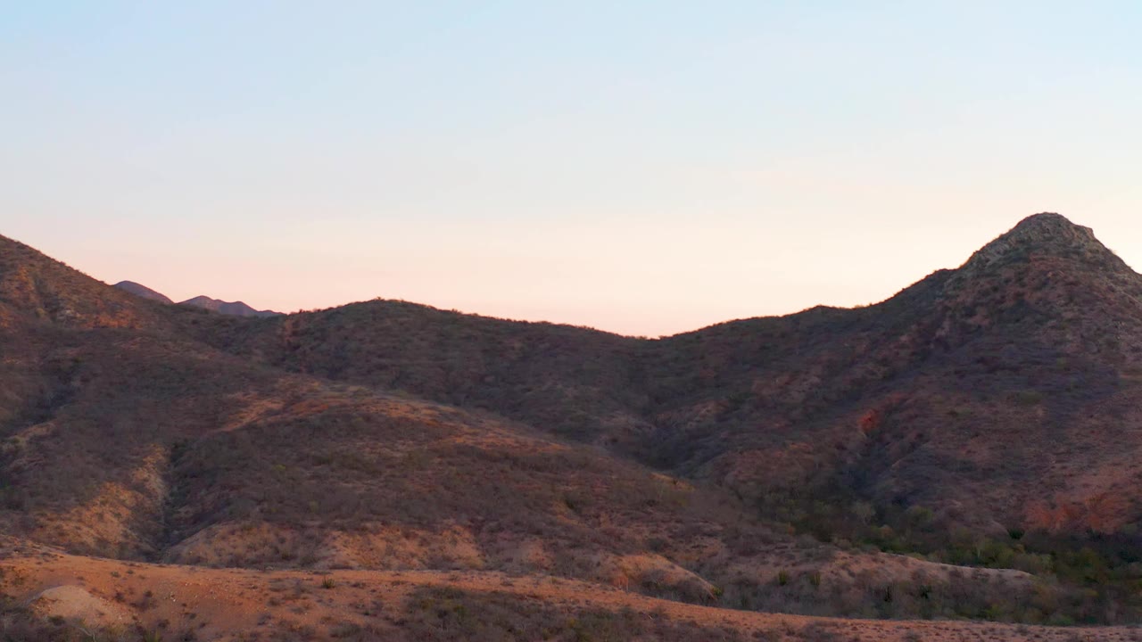 The central rocky peak sits slightly right of frame in Cabo Pulmo, with brown ridges, sparse desert vegetation, a dim valley line, and no visible people.