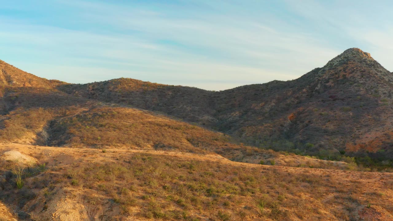 Wide arid terrain in Cabo Pulmo, Baja California Sur, with a scrubby foreground, layered brown hills, a rocky peak at right, and no visible people.