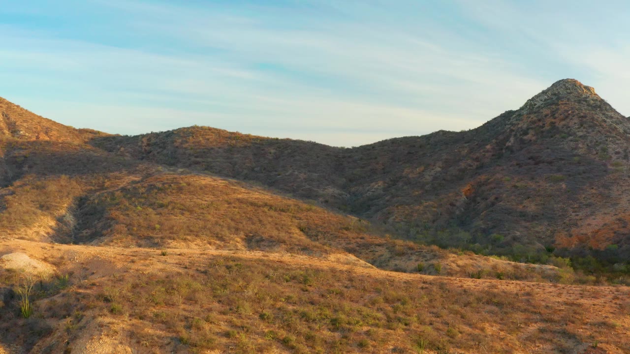 A sunlit dry slope leads into rocky hills in Cabo Pulmo, with the main rounded peak set to the right and no visible people in the frame.
