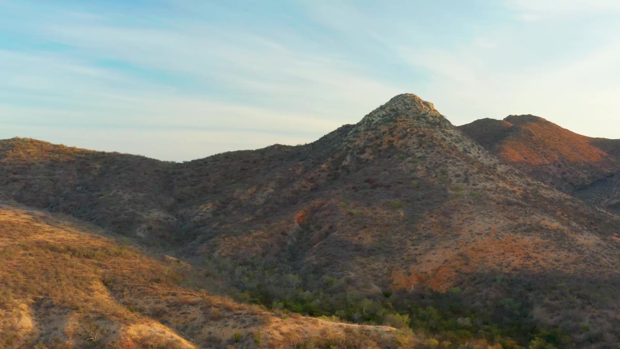 Cabo Pulmo mountain landscape with the central rocky peak slightly larger in frame, shadowed valley brush below, warm sun on side ridges, and no visible people.