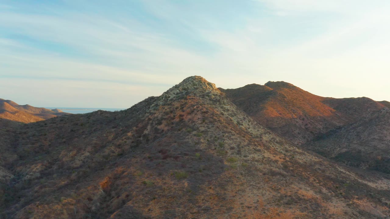 Aerial view of Cabo Pulmo arid slopes with the main peak shifting right in the frame, darker mountains behind it, and no visible people.
